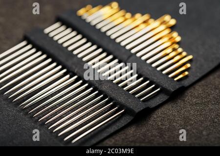 Gold sewing needles on a black background in a row. Stock Photo