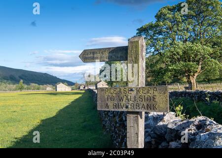 Signpost directing walkers to keep to the edge of a wildflower meadow, near Hubberholme, Wharfedale, Yorkshire Dales National Park, UK. Stock Photo
