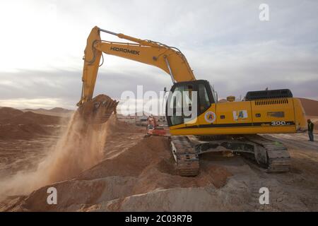 An excavator being used to remove sand to level the ground, part of the works to construct a large oil facility in the Sahara Desert. Stock Photo