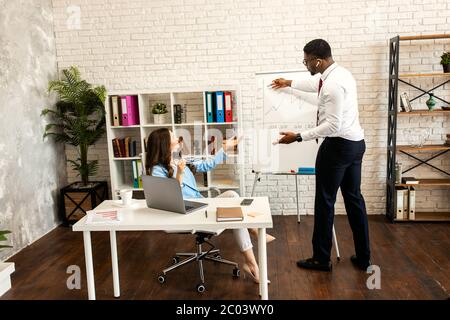 Photo of smiling young colleagues sitting in office coworking using laptop computers.  Stock Photo