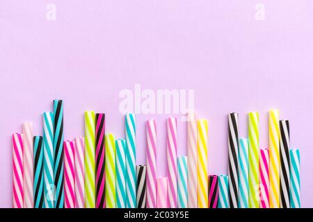 drinking straws with stripes for party on lilac background. Top view of colorful plastic tubes for summer cocktails. Flat lay Copy space Birthday Stock Photo