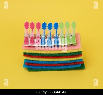 stack of new multi-colored kitchen sponges for washing dishes and clothespins on a yellow background, close up Stock Photo