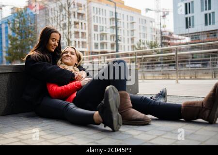 Happy Best Friends Embracing And Sitting On The Ground In City Stock Photo