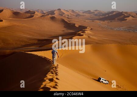 An office worker at a oil facility being developed in the Sahara desert, North Africa, walks  a high dune in the late afternoon. Stock Photo