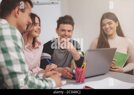 Cheerful handsome young male student smiling joyfully at his college friends, while studying together. Group of university students preparing for exam Stock Photo