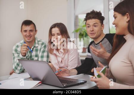 Cheerful college friends talking, while preparing for exams together at the library. Handsome male student talking to his classmates, working on a pro Stock Photo