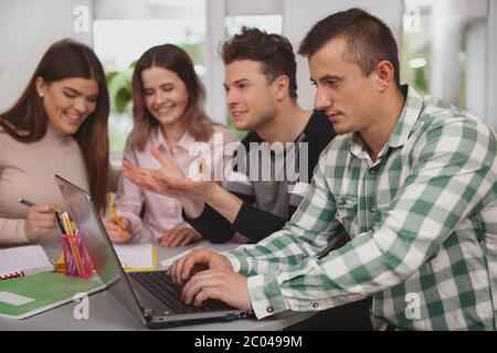 Communication, college concept. Young male student typing on laptop, working on group study project with his classmates Stock Photo
