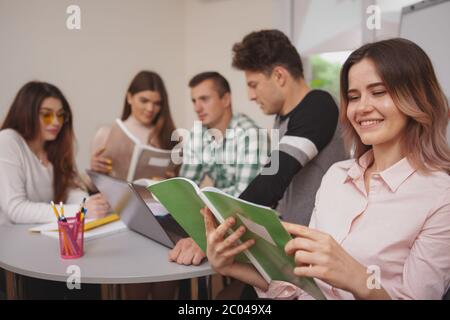 Education, learning concept. Charming young beautiful female student reading her notes in textbook, her college friend studying on the background, cop Stock Photo