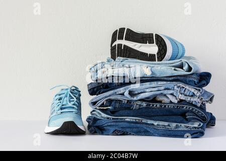 A stack of different jeans trousers and blue sneakers close up on white background, casual clothes , sports style Stock Photo