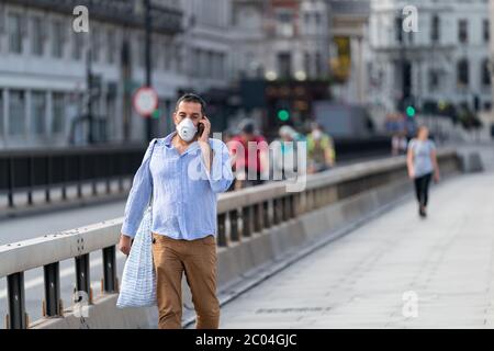Middle aged Middle Eastern Arabic man walking along Waterloo Bridge in London, England wearing a face mask and talking on his mobile phone Stock Photo