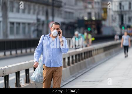 Middle aged Middle Eastern Arabic man walking along Waterloo Bridge in London, England wearing a face mask and talking on his mobile phone Stock Photo
