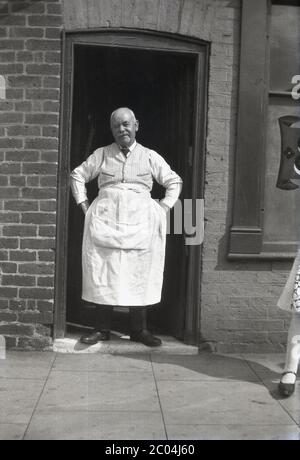 circa 1940s, historical, an elderly publican or pub landlord standing in the narrow doorway on a street showing off his large white apron, Rotherham or possibly Sheffield, England, UK. Stock Photo