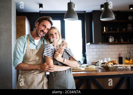 Beautiful young couple is talking and smiling while cooking healthy food in kitchen at home Stock Photo