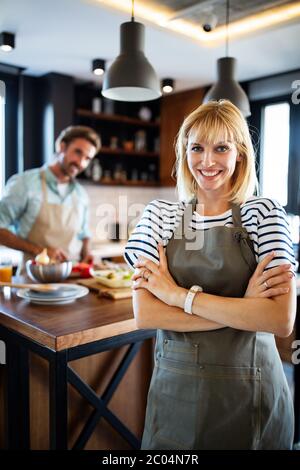 Beautiful young couple is talking and smiling while cooking healthy food in kitchen at home Stock Photo