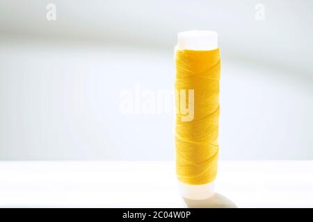 Yellow thread spool on a white bright table. Stock Photo