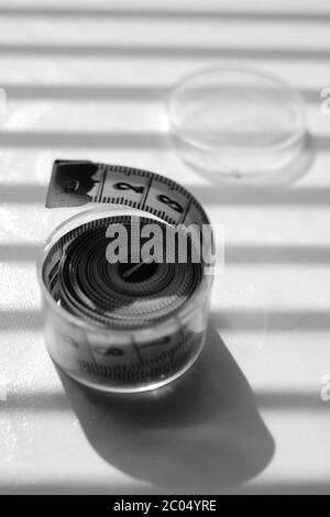 Tailor measuring tape in a plastic box on a shiny table. Black and white photo. Stock Photo