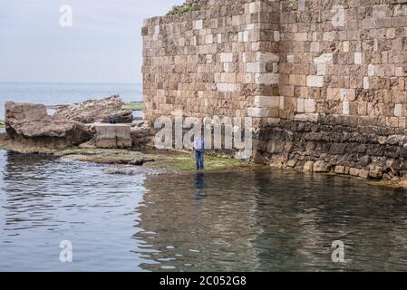 Angler next to ruins of ancient port in Byblos, largest city in the Mount Lebanon Governorate of Lebanon Stock Photo