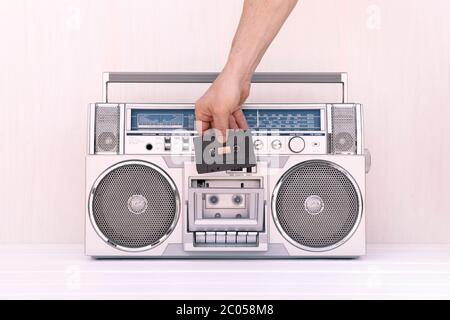 Hand inserting a tape of music into the deck of a vintage 80s radio cassette. Play music concept. Stock Photo