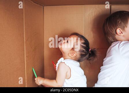 Beautiful little children draw with felt-tip pens and play in box, activity for children at home Stock Photo