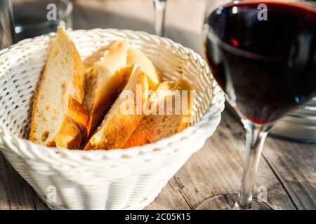 Baguette slices in white wicker basket and a glass of red wine on wood table at a French cafe terrace Stock Photo