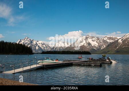 Boaters on Jackson Lake at Colter Bay with the snow capped Teton Mountain Range behind during spring at Grand Teton National Park in Moose, Wyoming. Stock Photo