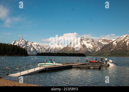 Boaters on Jackson Lake at Colter Bay with the snow capped Teton Mountain Range behind during spring at Grand Teton National Park in Moose, Wyoming. Stock Photo