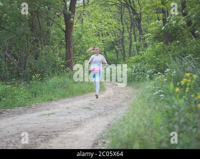 Young Blonde Caucasian Female Running in Forest on a Dirt Road Stock Photo