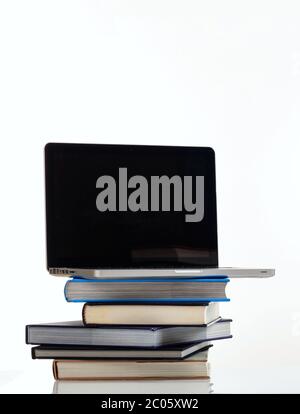 E learning concept. Books stack and an open computer laptop with black blank screen isolated on white background. Vertical photo, copy space, template Stock Photo