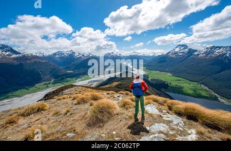 Hiker on the summit of Mount Alfred, view into the valley of the Dart River, snow-covered peaks of the New Zealand Alps, Glenorchy near Queenstown Stock Photo