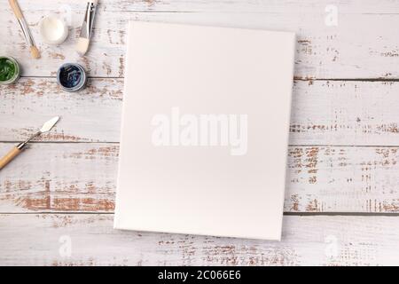 Colorful creative table with blank canvas for sketches and paints, paintbrushes set on white wooden table, top view, copy space, flat lay style, drawi Stock Photo