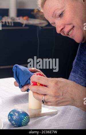 sorbian redhead Women's hands remove with a candle flame the wax according to Sorbian tradition of the red multicolored Easter egg Stock Photo
