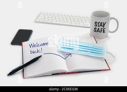 Welcome back to work concept. Medical protection mask waiting at the desk along with note pad, computer keyboard, phone, pencil and a coffee mug. Read Stock Photo