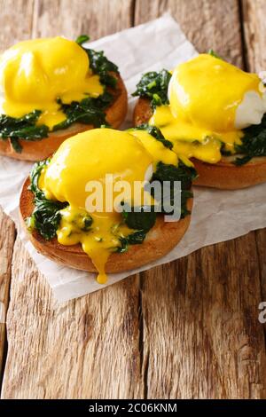 Breakfast of poached eggs with spinach and hollandaise sauce on bread close-up on the table. vertical Stock Photo