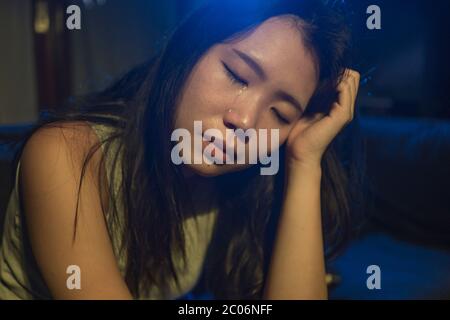 young beautiful sad and depressed Asian Korean woman crying in tears on darkness in pain feeling worried and helpless sobbing desperate at living room Stock Photo