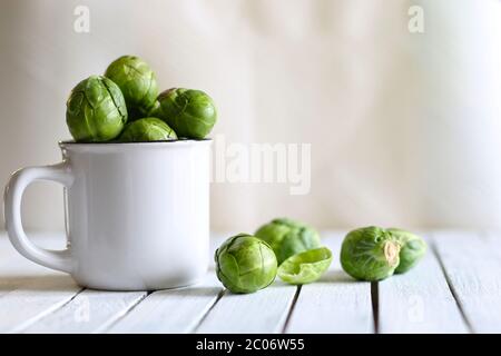 Vegetable concept. Fresh organic Brussels sprouts in a white bowl on a wooden table. Blurry background. Stock Photo