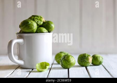 Vegetable concept. Fresh organic Brussels sprouts in a white bowl on a wooden table. Blurry background. Stock Photo