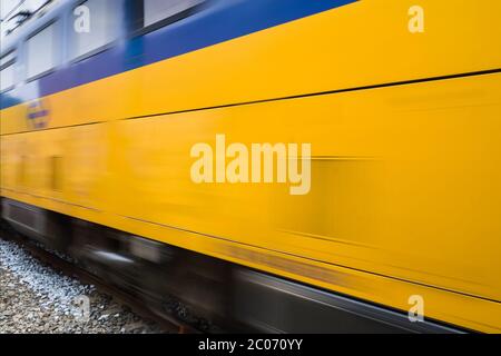 Dutch train with distinctive yellow and blue color passing by on a railway in Heerenveen in the Netherlands Stock Photo