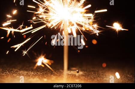 Close-up of golden blurry sparks burn in the dark from the light of festive candles. The concept of fireworks and congratulations on the holidays and Stock Photo