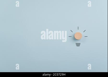 Light bulb made of wooden cut circle and hand drawn rays on the right side of an image with plenty of copy space to the left. Over light blue backgrou Stock Photo