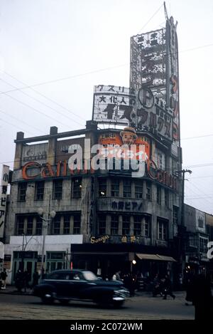 [ 1950s Japan - Tokyo Ginza ] — Advertising signs on the head office of Ono Piano, one block away from the Ginza 4-chome intersection in Tokyo, ca. 1953 (Showa 28).  Around the corner was the gay café Brunswick, frequented by Japanese authors Yukio Mishima and Edogawa Ranpo. Japanese singer Akihiro Miwa worked there as a ‘boy’.  The sign above the Canon camera advertises Charlie Chaplin’s movie Limelight, which was released in Japan on February 18, 1953.  20th century vintage slide film. Stock Photo