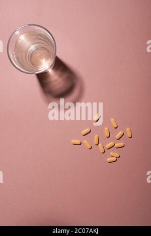 Group of yellow pills and glass of water on a pink background, top view Stock Photo