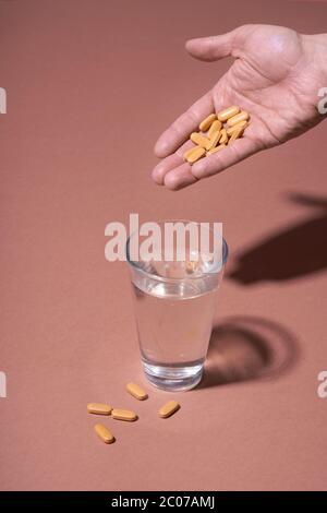 Human hand holding pills and glass of water on coral background Stock Photo
