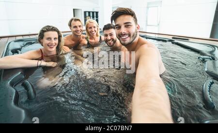 Happy friends taking selfie while doing jacuzzi in luxury house - Young people having fun together in hot tub Stock Photo