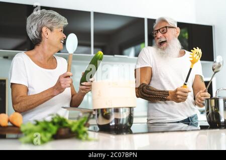 Happy senior couple having fun cooking together at home - Elderly people preparing lunch in modern kitchen Stock Photo