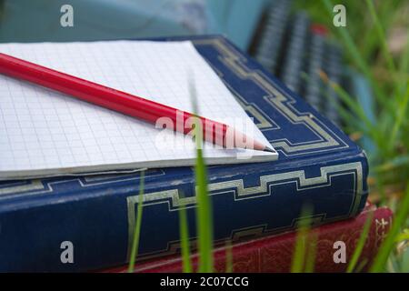 Notepad, pencil and old books on the green grass Stock Photo