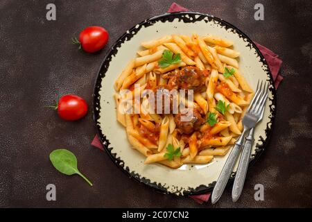 Meatballs in tomato sauce with penne pasta on a dark rustic background. Top view, flat lay, copy space