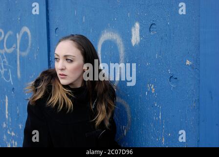 Authentic portrait of young woman against urban blue background. Stock Photo