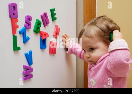 Early years childhood development. One year old girl playing with magnetic fridge letters. Stock Photo