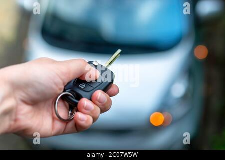 Women hand hand holding contactless car key and pressing the button on the remote to lock or unlock the car. Flashing lights of the car Stock Photo