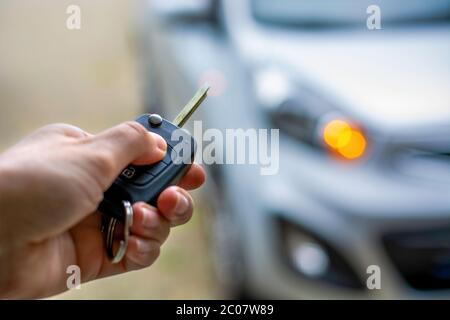 Women hand hand holding contactless car key and pressing the button on the remote to lock or unlock the car. Flashing lights of the car Stock Photo